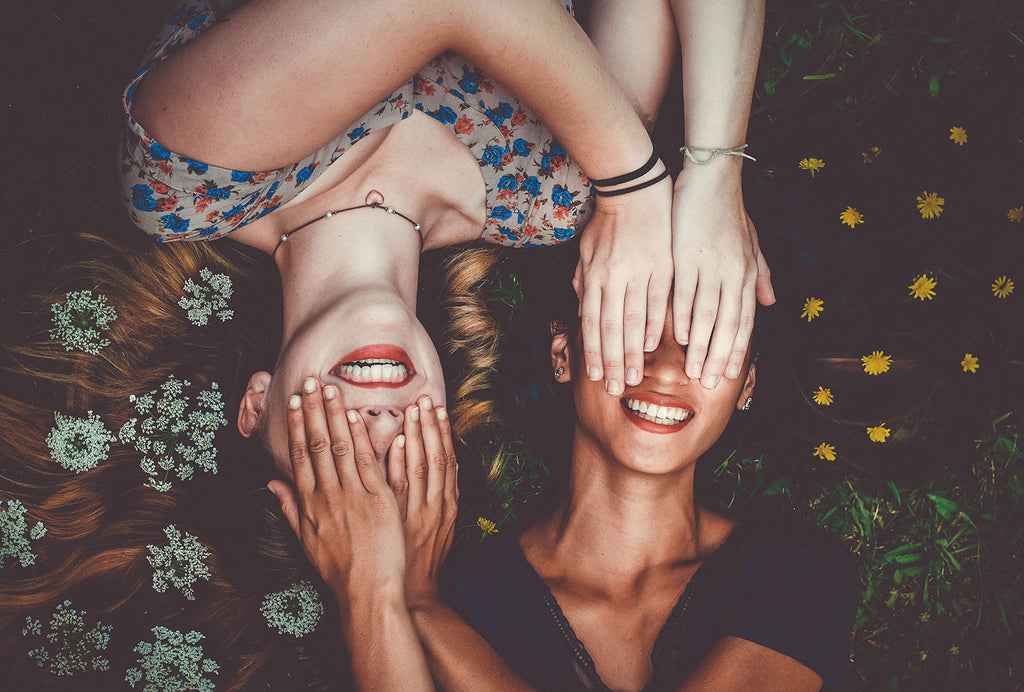 Two smiling women with hands over their eyes. 